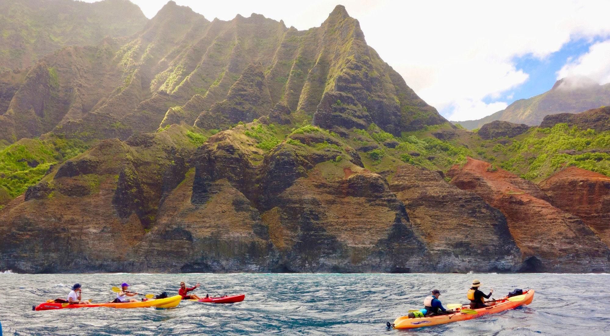 Sea kayaks dwarfed by the ridgeline of the Na Pali Coast