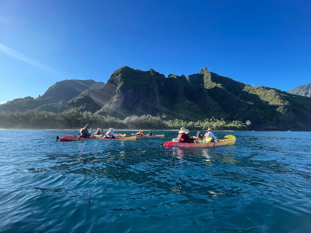 A Na Pali Kayak group paddling off Hā'ena on a clear summer morning
